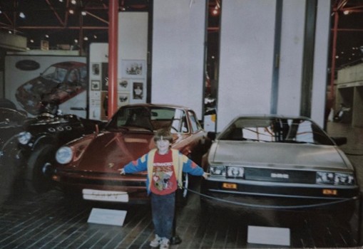 Porsche 911 & DMC DeLorean Chris stands between a red Porsche 911 and a silver DMC DeLorean at Beaulieu National Motor Museum