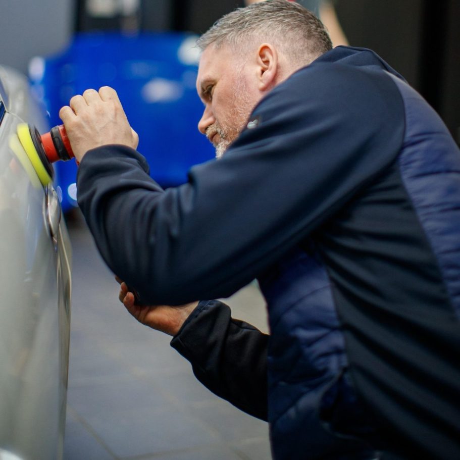 Man polishing a car's surface with a buffer in a garage setting.