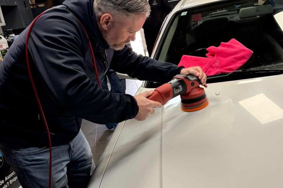 Back to Fresh Stage 2 Detail A man uses a polishing machine on a car's surface in a workshop setting.