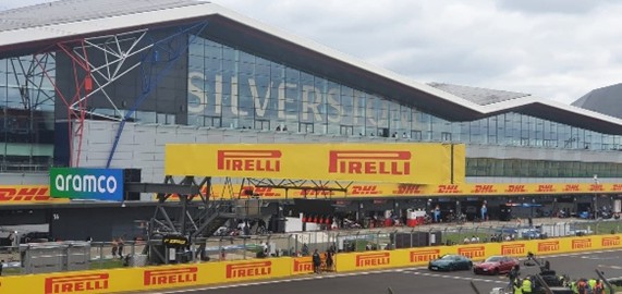 Silverstone 2021 Silverstone circuit's grandstand with Pirelli banners and Formula 1 cars in the foreground.